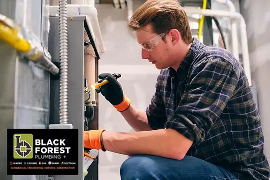 A plumber wearing safety glasses and orange gloves works on a furnace or boiler with a tool. The Black Forest Plumbing logo is visible in the bottom left corner.